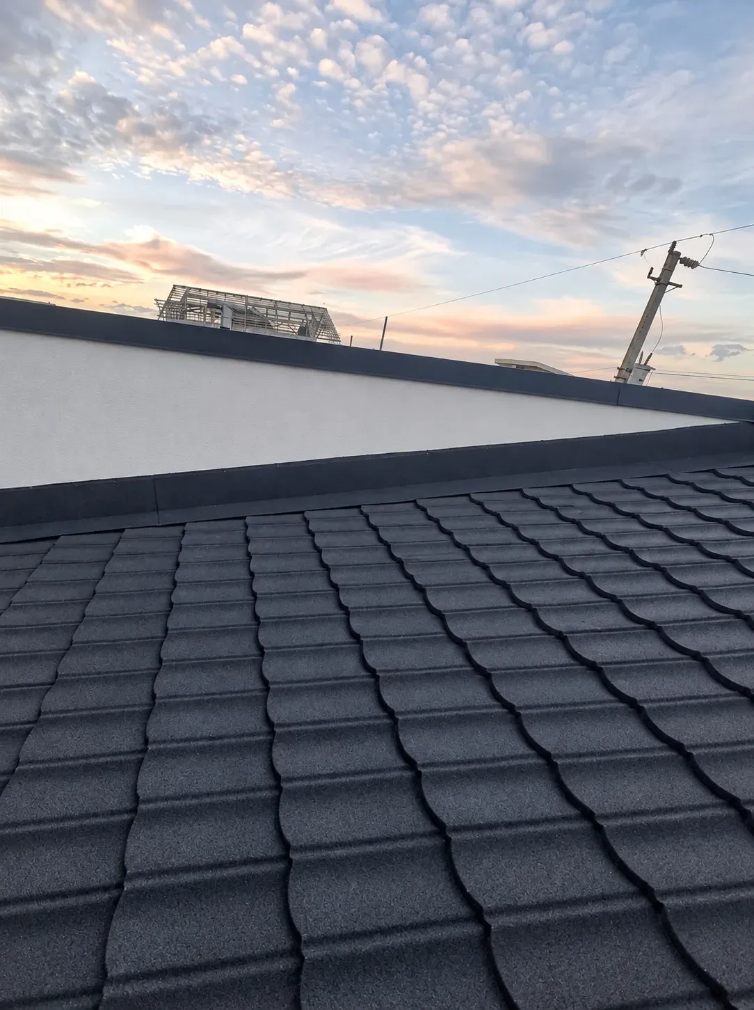 Techo de teja negra recubierta con piedra, con remates contra un muro blanco, al atardecer